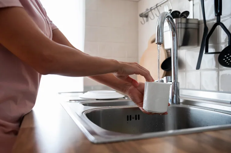 Hand rinsing a white mug at a kitchen sink